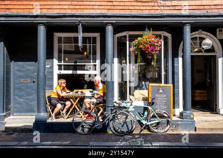 Deux cyclistes seniors assis devant Un café avec Un café, High Street, Lewes, East Sussex, Royaume-Uni. Banque D'Images