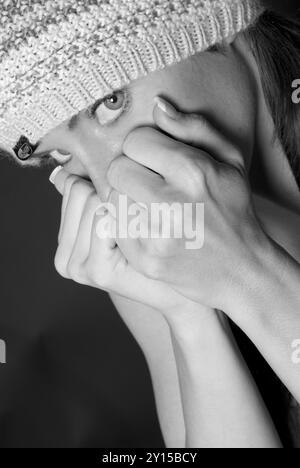 Femme caucasienne effrayée (20-25 ans) portant une casquette de luge, couvrant sa bouche avec les poings fermés, exprimant des symptômes d'anxiété. ÉTATS-UNIS. Banque D'Images