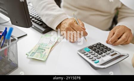 Un homme d'âge moyen compte les roubles russes dans un bureau, avec une calculatrice et un stylo à la main pour l'analyse financière. Banque D'Images