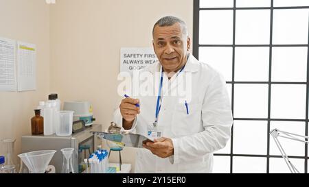 Un homme hispanique d'âge moyen portant une blouse de laboratoire écrivant sur un bloc-notes dans un laboratoire d'hôpital. Banque D'Images