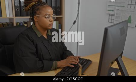 Femme travaillant dans un bureau de juge tapant sur un clavier portant des lunettes et des robes judiciaires, ce qui implique un cadre de tribunal officiel Banque D'Images