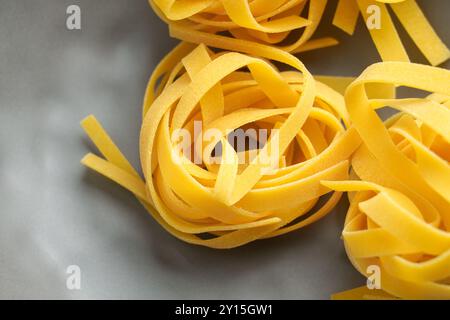 Pâtes fettuccine italiennes crues à partir de blé biologique dans un bol en céramique grise gros plan. Ingrédient nutritif non cuit. Banque D'Images