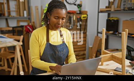 Femme africaine utilisant un ordinateur portable dans un atelier de menuiserie, axé sur une tâche Banque D'Images