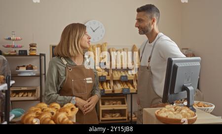 Homme et femme dans des tabliers parlant à l'intérieur d'une boulangerie avec des étagères de pain en arrière-plan Banque D'Images