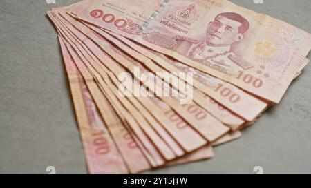 Des billets de banque thaïlandais de différentes quantités sont affichés sur une surface en béton, soulignant le design et la monnaie distincts du baht thaïlandais. Banque D'Images