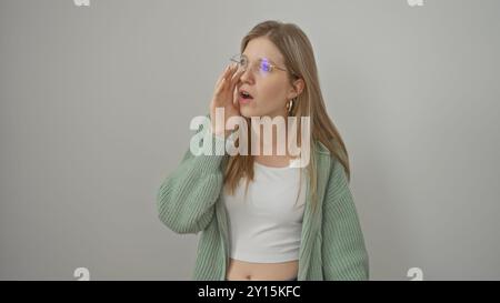 Jeune femme adulte aux cheveux blonds portant des lunettes et un pull vert sur un dessus blanc isolé sur un fond blanc. Banque D'Images