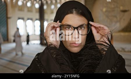 Jeune femme hispanique adulte en lunettes dans une mosquée de doha, présentant l'architecture islamique et le tourisme culturel qatari. Banque D'Images