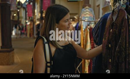 Une jeune femme brune explore les vêtements traditionnels dans un souk de dubaï, immergeant dans la culture émiratie. Banque D'Images