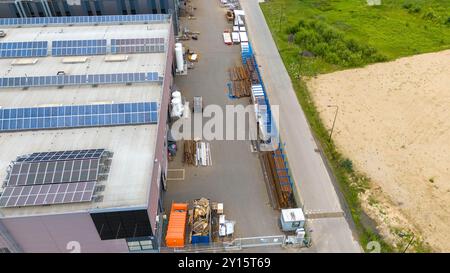 Une vue aérienne d’une zone industrielle avec un entrepôt avec panneaux solaires sur le toit, un large chemin bordé de matériaux de construction et d’équipements Banque D'Images