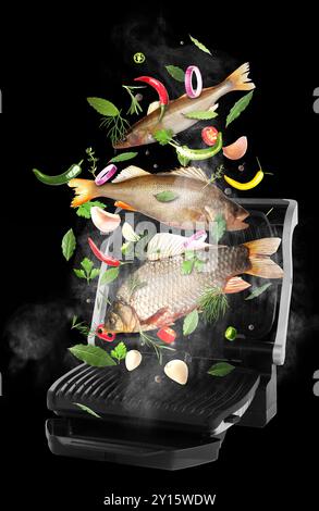 Fruits de mer, légumes, herbes et épices tombant sur le gril électrique sur fond noir. Repas de cuisine Banque D'Images