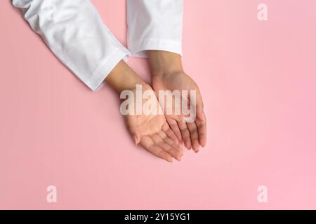 Les mains d'un médecin féminin dans un manteau blanc, paumes vers le haut, se trouvent sur la table sur un fond rose Uni - photo Banque D'Images