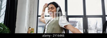 Une femme heureuse aime la musique tout en dansant dans un espace intérieur élégant. Banque D'Images