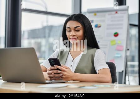 Une femme confiante aime une conversation sur son smartphone tout en travaillant. Banque D'Images