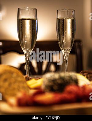 Deux verres de champagne avec plateau de fromage au premier plan et éclairage romantique en arrière-plan Banque D'Images