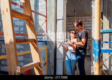 Jeune couple marié vérifiant leur future maison en construction. Famille imagine leur maison debout près d'un mur fait de bloc de gaz tenant le papier flou Banque D'Images