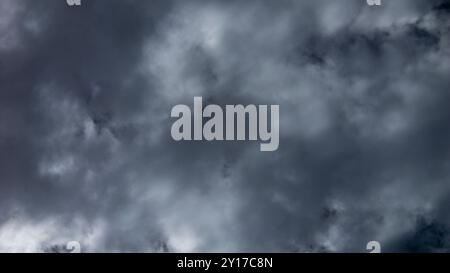 Des nuages tempêtes denses et sombres se dessinent au-dessus du ciel, projetant des ombres sur une zone rurale sereine alors que la lumière de l'après-midi commence à s'estomper, signalant le risque de pluie. Banque D'Images