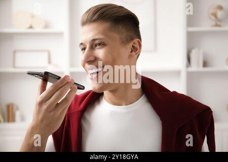 Jeune homme enregistrant un message vocal via smartphone à la maison Banque D'Images