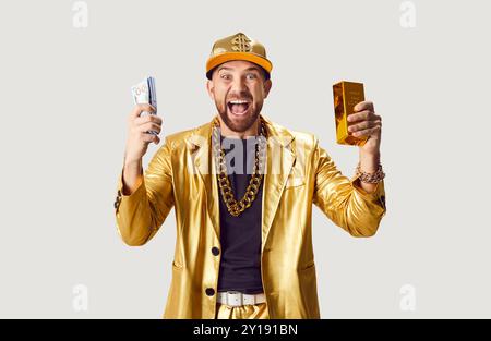 Portrait de l'homme riche en costume d'or tenant de l'argent comptant et barre d'or sur fond blanc Banque D'Images