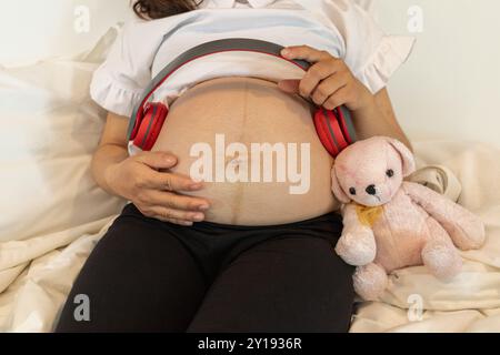 Flou et fluidité de la mise au point, Une mère enceinte tient un casque dans sa main et couvre son utérus pour jouer de la musique pour son enfant à naître, croyant que le cla Banque D'Images