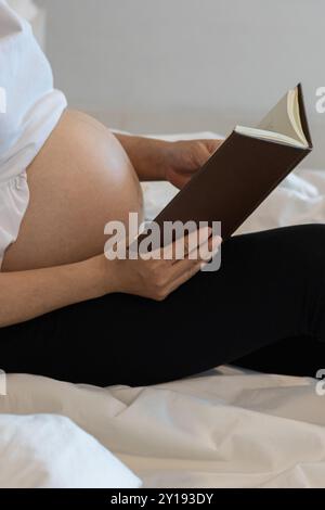 Soft Focus et Smooth Focus,la mère de grossesse se trouve seule dans sa chambre à coucher en lisant sur le lit pour étudier les soins du nouveau-né du livre pendant la grossesse donc Tha Banque D'Images