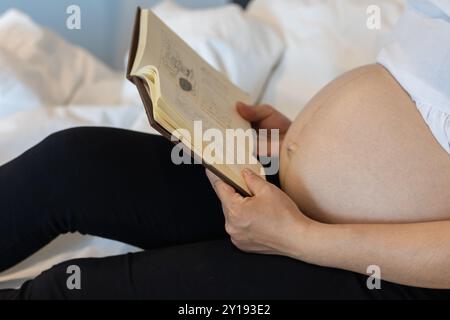 Soft Focus et Smooth Focus,la mère de grossesse se trouve seule dans sa chambre à coucher en lisant sur le lit pour étudier les soins du nouveau-né du livre pendant la grossesse donc Tha Banque D'Images