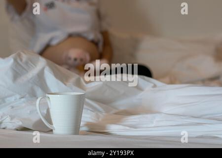 Une tasse à café en céramique blanche a été placée sur le lit dans la chambre le matin après que la tasse ait été consommée. Une tasse en céramique blanche pour thé chaud et co Banque D'Images