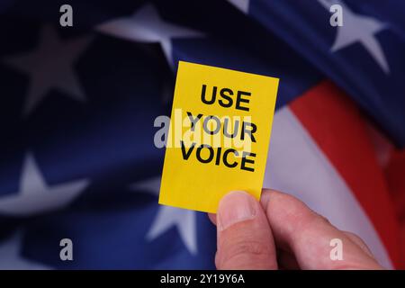 Une main tenant une note de papier jaune avec le slogan Use Your Voice dessus devant le drapeau des États-Unis. Banque D'Images