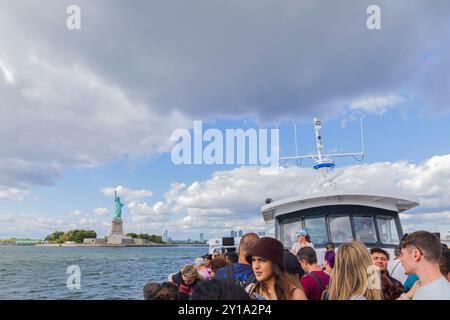 Groupe de touristes sur le ferry approchant l'emblématique Statue de la liberté dans le port de New York. New York. ÉTATS-UNIS. Banque D'Images