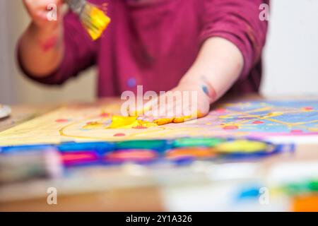 Gros plan des mains d'un enfant peignant un morceau de papier avec un pinceau et ses mains. Banque D'Images