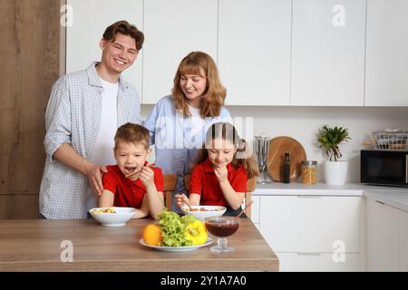 Petits enfants avec leurs parents prenant le petit déjeuner avant l'école dans la cuisine Banque D'Images