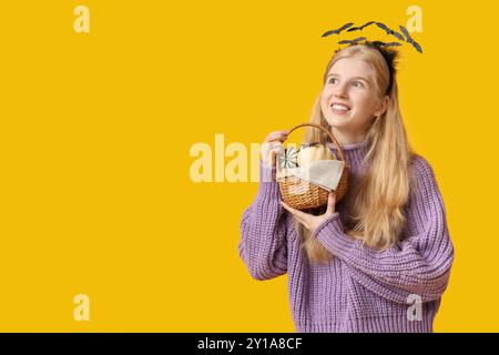 Belle jeune femme heureuse dans le bandeau avec panier en osier de citrouilles d'Halloween sur fond jaune Banque D'Images