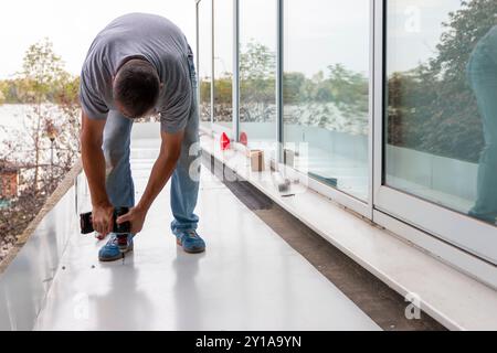 Travailleur de la construction installant un nouveau toit en tôle. Homme avec perceuse sans fil visse la feuille de toiture au toit d'une maison. Banque D'Images