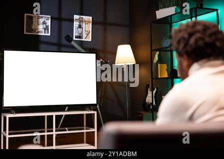 Homme BIPOC regardant la compétition de football basée sur abonnement en direct sur écran isolé Smart TV. Propriétaire sur le canapé devant la maquette d'un téléviseur divertissant par un match de football Banque D'Images