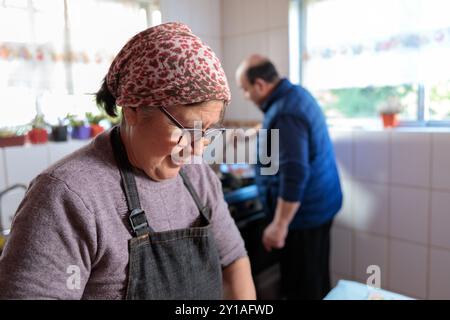 Gros plan d'une senior latine souriante cuisinant et préparant un repas avec son mari dans leur cuisine traditionnelle Banque D'Images