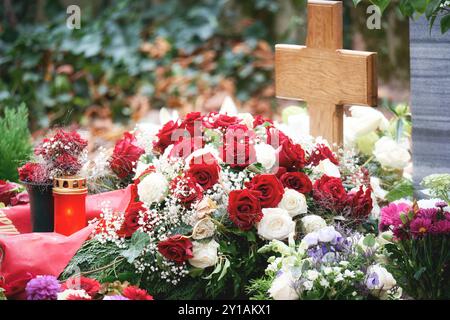 bouquet de roses blanches et rouges avec ruban rouge et lumière de tombe sur une tombe avec croix en bois non marquée Banque D'Images