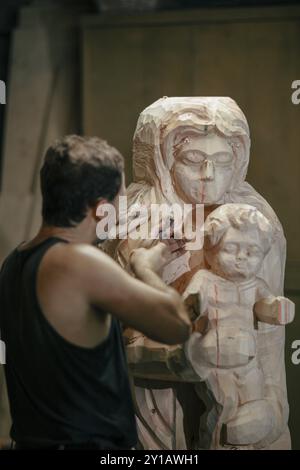 Homme sculptant habilement une statue en bois dans un atelier, équipé de divers outils Banque D'Images