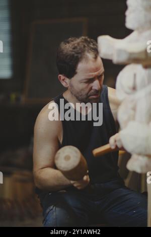 Un artisan sculpte une statue en bois avec précision dans un atelier Banque D'Images