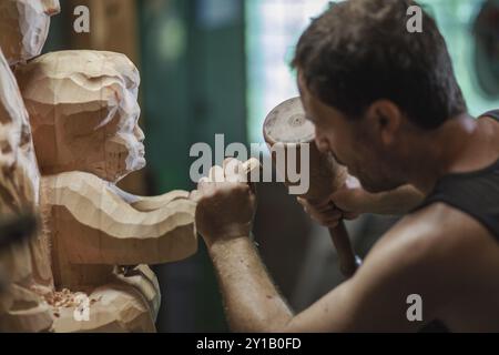 Un artisan sculptant méticuleusement une statue en bois dans un atelier, mettant en valeur son talent et sa concentration Banque D'Images