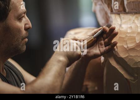 Un menuisier cisaille intensément une grande figure en bois, en se concentrant sur les détails complexes Banque D'Images