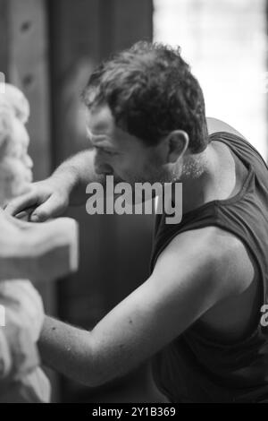 Un artiste s’est intensément concentré sur la sculpture d’une sculpture en bois, capturée dans une photographie en noir et blanc Banque D'Images