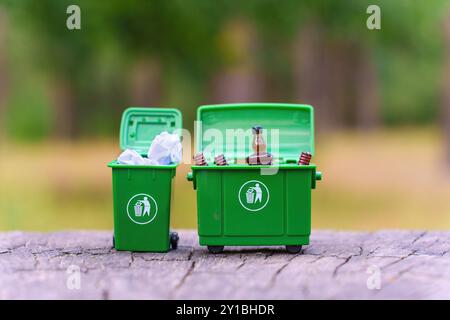 Deux poubelles vertes miniatures ouvertes remplies de déchets, exposées sur une surface en bois à l'extérieur. Pratiques de recyclage et homme responsable des déchets Banque D'Images