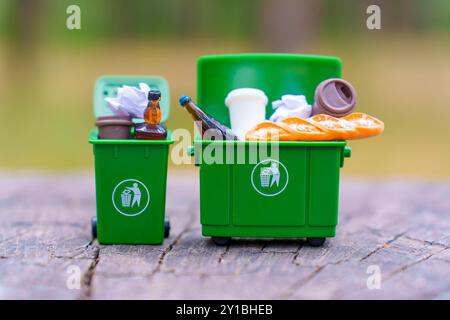 Deux poubelles miniatures vertes remplies de divers déchets, soulignant l'importance de la séparation dans le recyclage des déchets. Banque D'Images