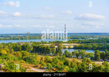 Vue grand angle de la zone de construction près d'une rivière, avec grues et verdure, mettant en valeur le développement dans un paysage urbain. Banque D'Images