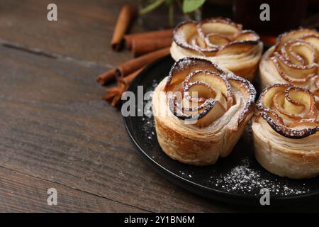Roses de pomme fraîchement cuites et bâtonnets de cannelle sur la table en bois, gros plan. Espace pour le texte Banque D'Images