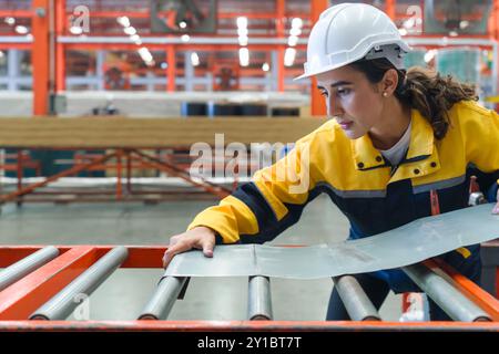 Jeune femme hispanique travail habillée en uniforme de veste de polyester et casque de protection travaillant dans la fabrication de tôle. Banque D'Images