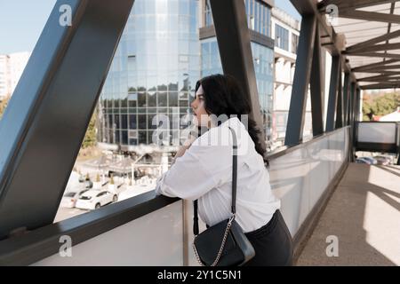 Femme d'affaires réfléchie contemplant le paysage urbain depuis le pont piétonnier moderne. Banque D'Images