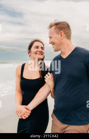 Couple marchant sur la plage, souriant l'un à l'autre, se tenant la main Banque D'Images