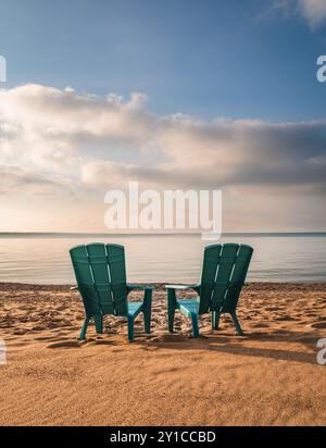 Deux chaises adirondack turquoise sur la plage de sable avec vue sur le lac en été. Banque D'Images