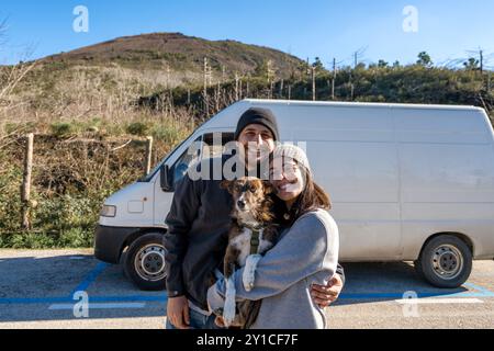 Couple regardant et souriant à la caméra avec leur chien et un camping-car Banque D'Images