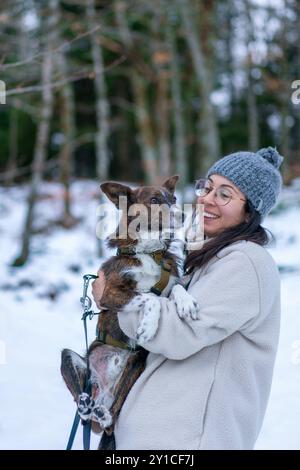 Jeune femme tenant et souriant au chien brun mignon sur un paysage de neige Banque D'Images